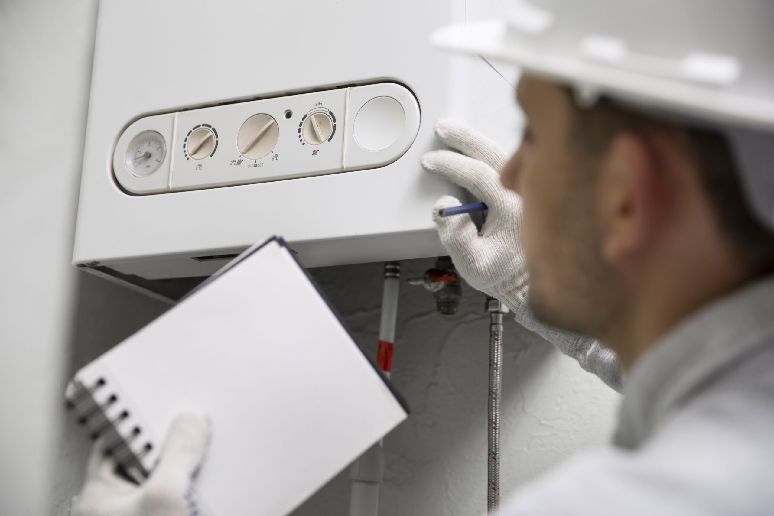 A heating engineer carrying out a boiler service and holding a service schedule in his hand.